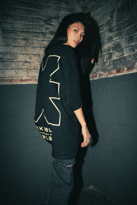Frau im schwarzen T-Shirt mit KKLBLxGWLS Logo und Print, Seitliche Ansicht aus GWLS x KKLBL