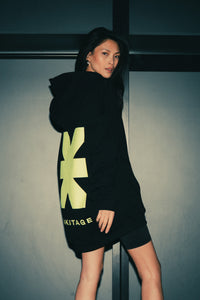 Frau im schwarzen Hoodie mit neongelbe KKLBLxGWLS Logo und Print, Seitliche Ansicht aus GWLS x KKLBL