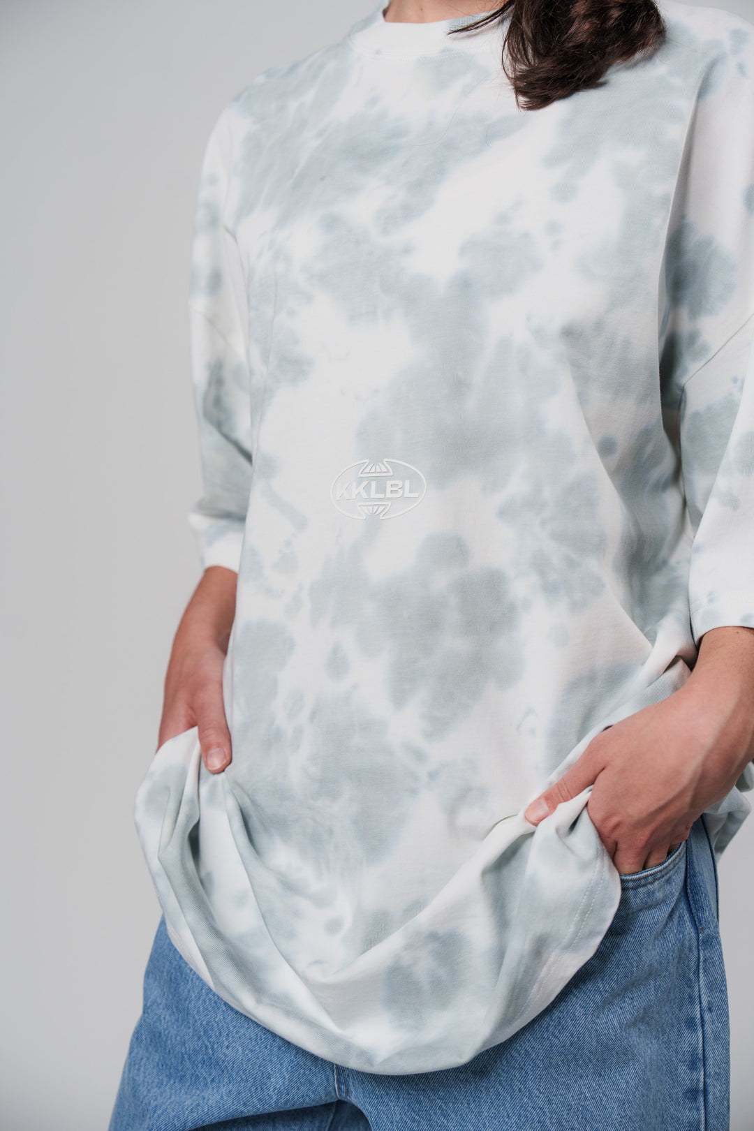 Frontalansicht:  Frau im hellblauen T-Shirt Tie Dye mit KKLBL Print aus Out of the Blue Collection