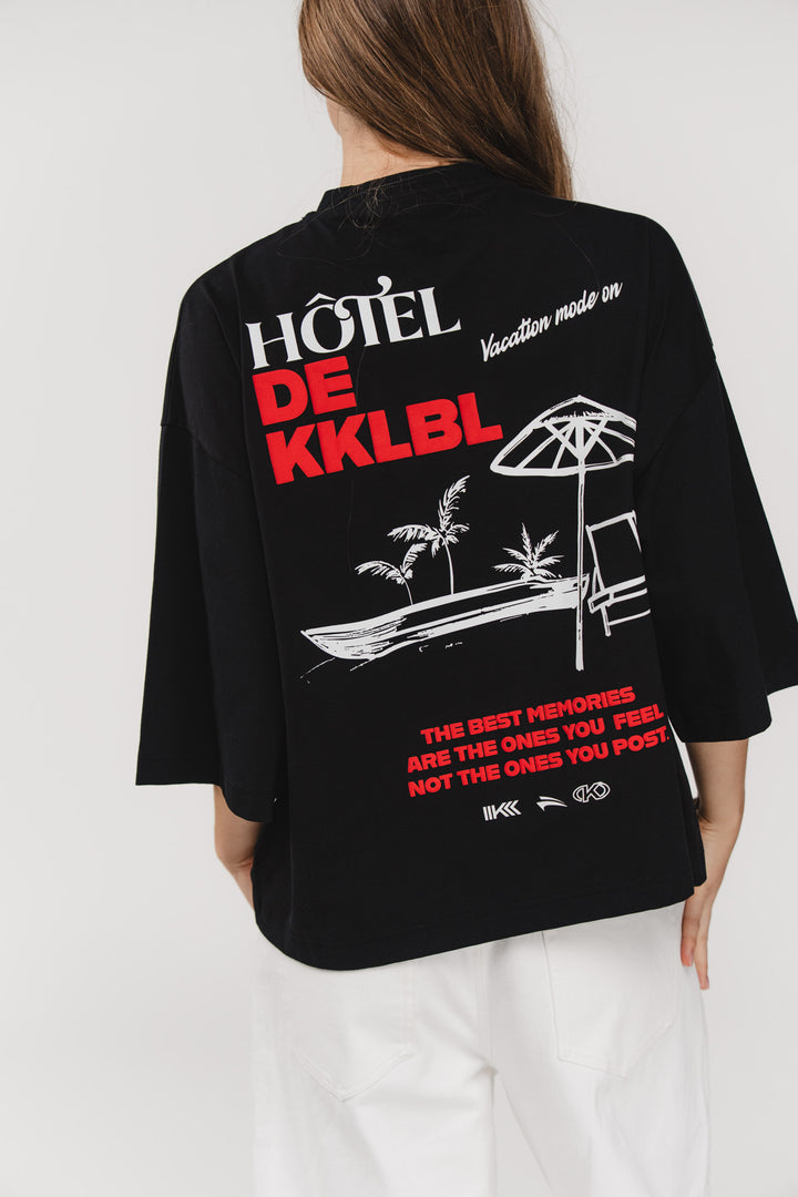 T-Shirt Cropped Vacation, Halbkörper schräg hinten, schwarzes Cropped-Shirt, großer Hotel de KKLBL Print