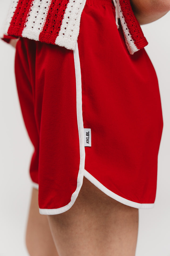 Track Shorts Red, Detailaufnahme seitlich, weißer Kontrastrand mit Weblabel als Marken-Detail