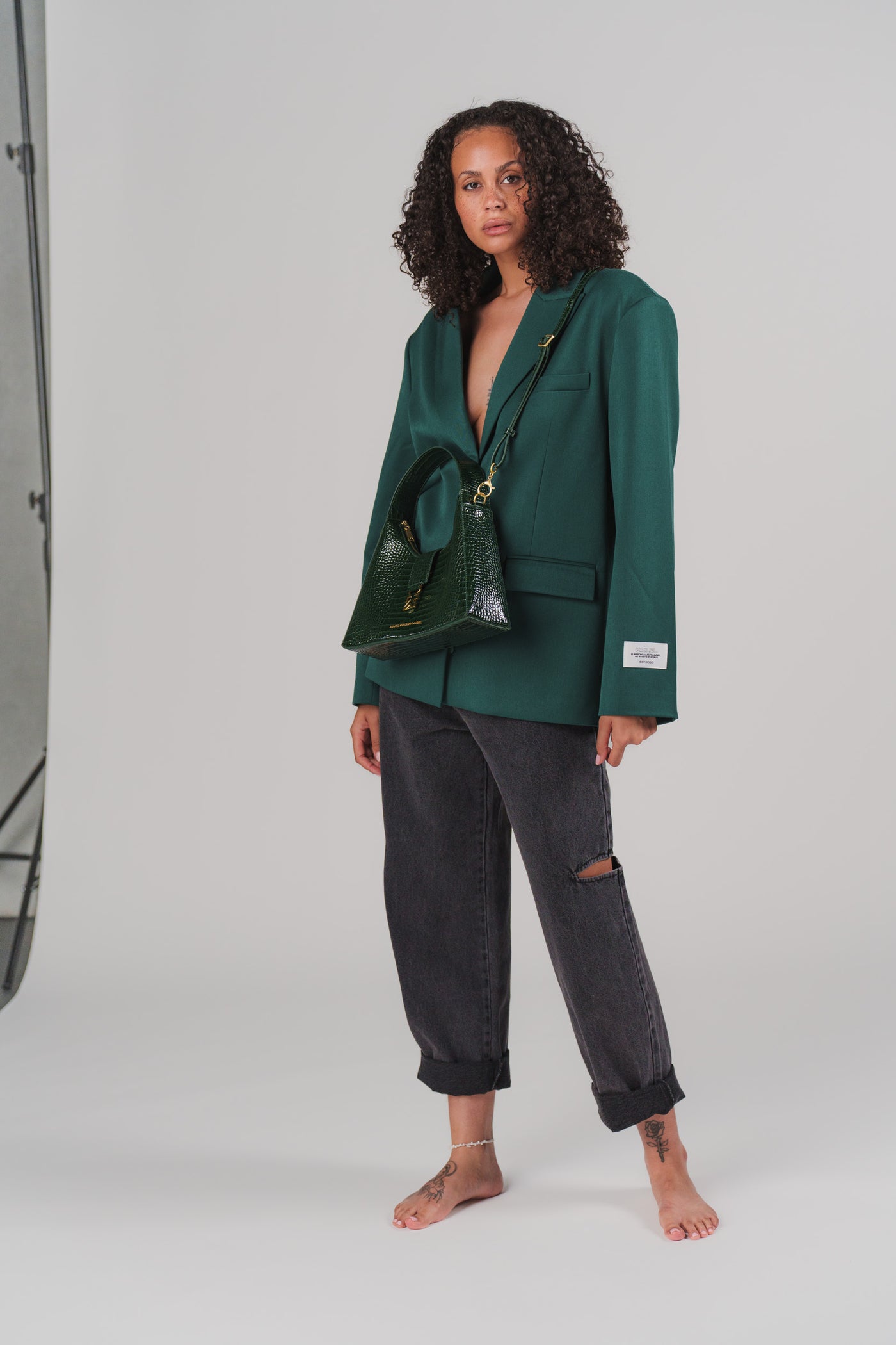 Ganzkörperaufnahme: Frau in lässiger Pose trägt dunkelgrünen Blazer und grüne Kroko-Handtasche aus der Evergreen Collection