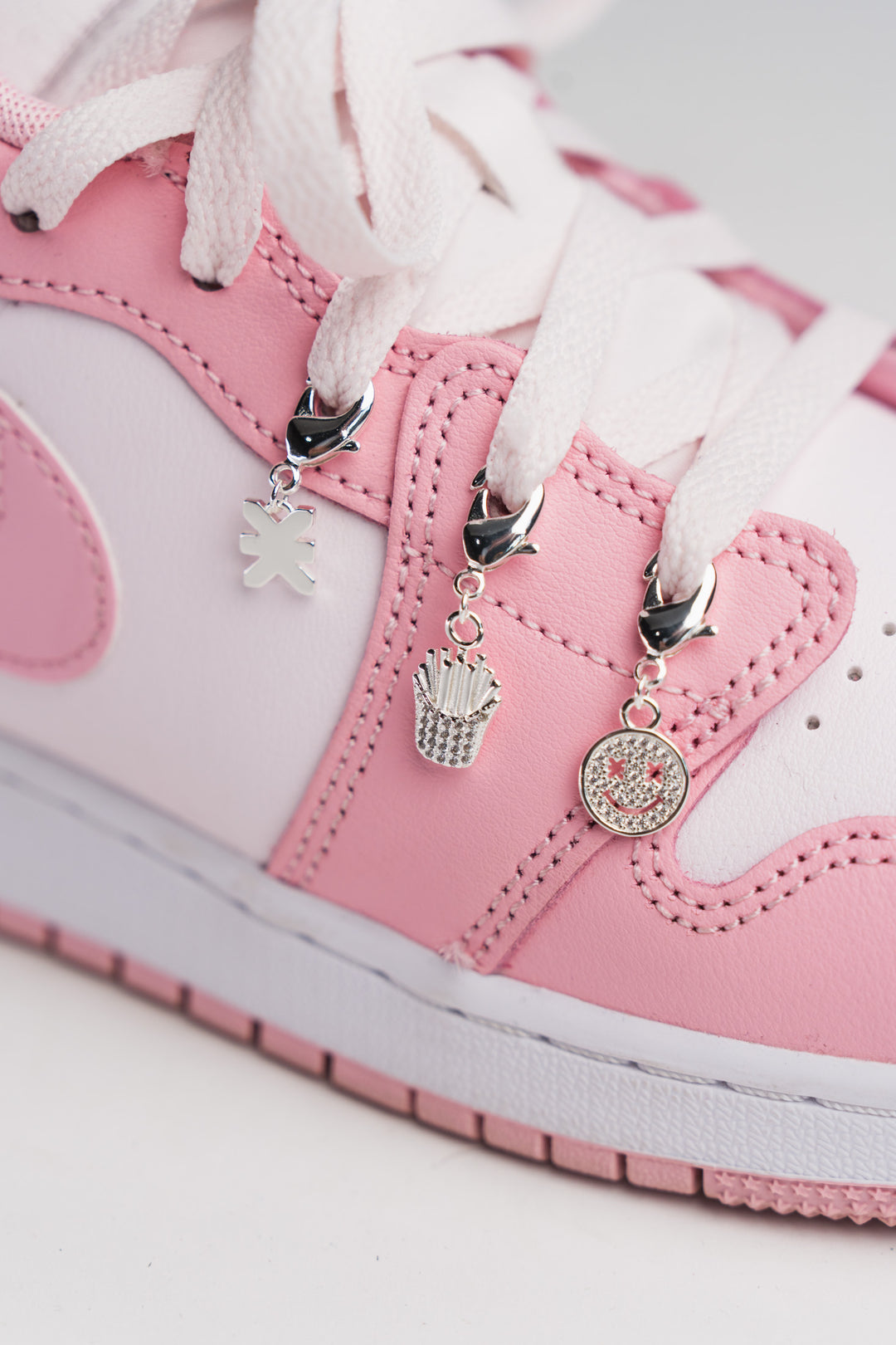 Charm Set Silver, Detailaufnahme drei silberne Charms an rosa Sneaker, Smiley, Pommes-Frites und KKLBL-Logo