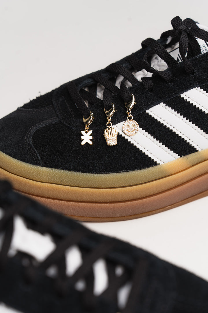 Charm Set Gold, Nahaufnahme goldene Anhänger-Charms mit Karabiner an schwarzem Sneaker-Schnürsenkel