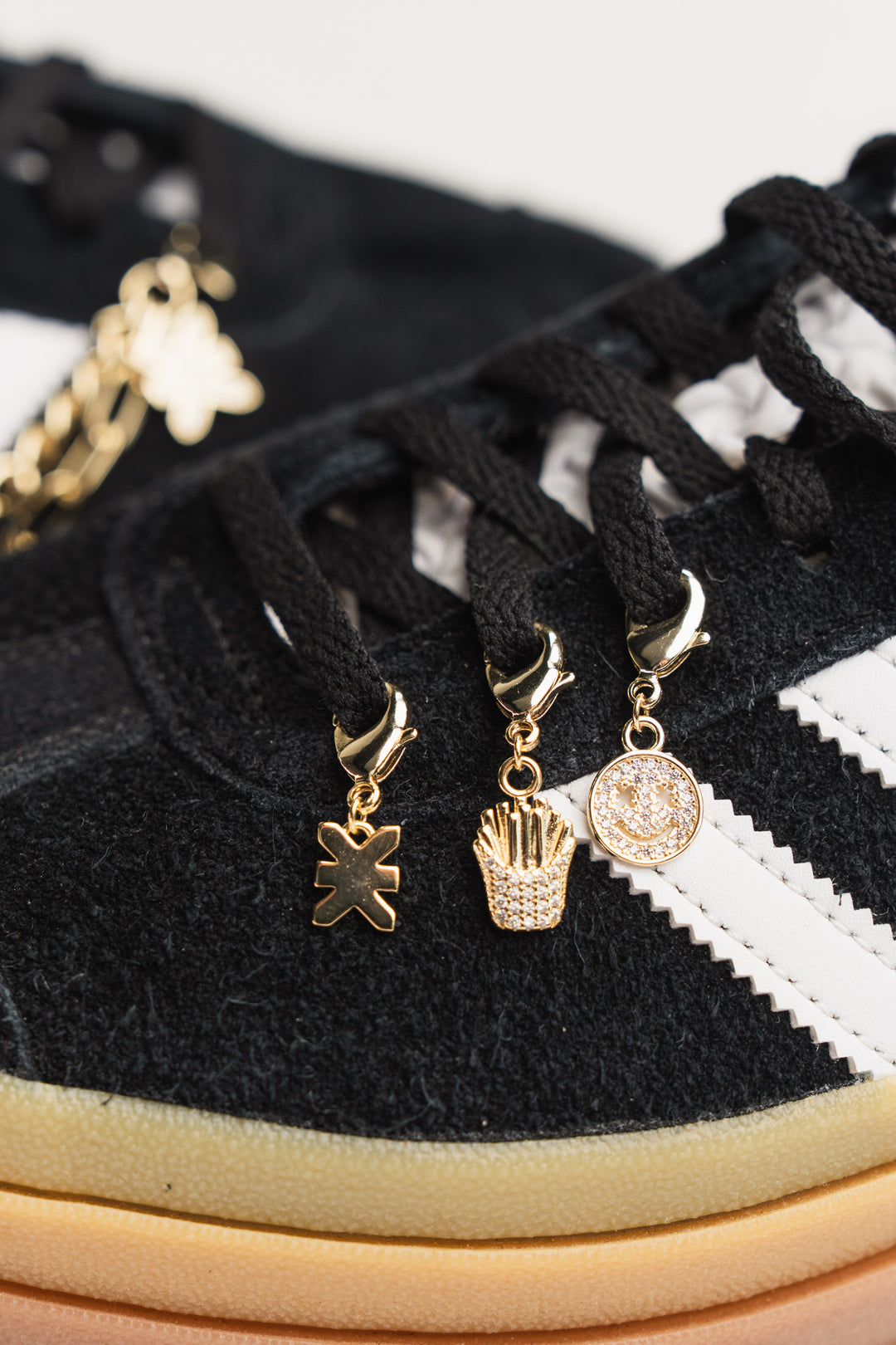 Charm Set Gold, Detailaufnahme drei goldene Charms an schwarzem Sneaker, Smiley, Pommes-Frites und KKLBL-Logo