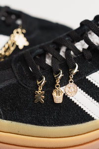 Charm Set Gold, Detailaufnahme drei goldene Charms an schwarzem Sneaker, Smiley, Pommes-Frites und KKLBL-Logo