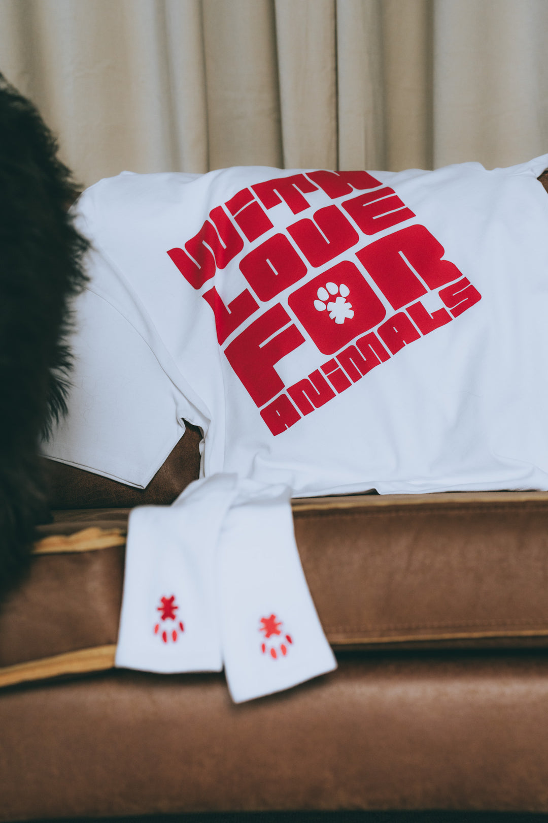 Produktaufnahme: Weißes T-Shirt mit rotem 'WITH LOVE FOR ANIMALS' Print auf Sofa