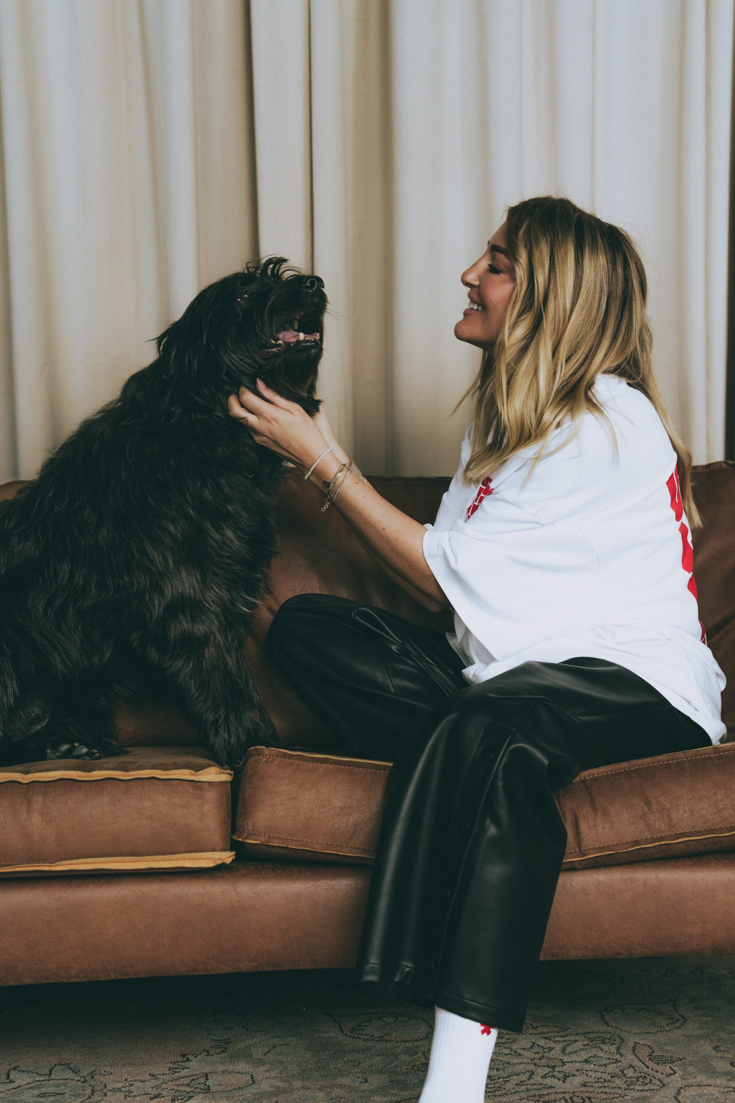 Frau im weißen T-Shirt mit rotem Print kuschelt mit schwarzem Hund, sitzende Pose
