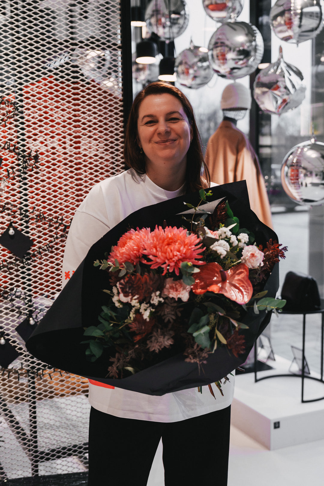 Frau im weißen Kommunity T-Shirt Pink mit Blumenstrauß, lächelnd in Frontalansicht