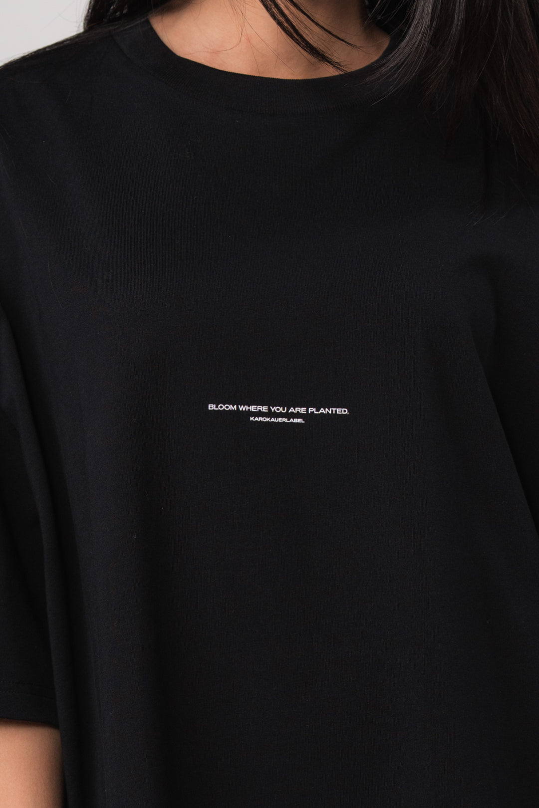 Detailaufnahme: Frau im schwarzen Oversized T-Shirt mit 'Bloom Where You Are Planted' Print