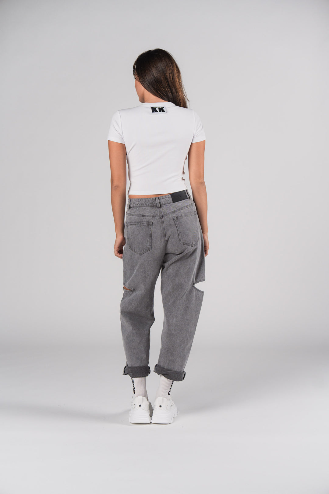 Rückansicht: Frau in weißem T-Shirt mit KK Print und grauen Denim Pants Grey Cut Out Petite