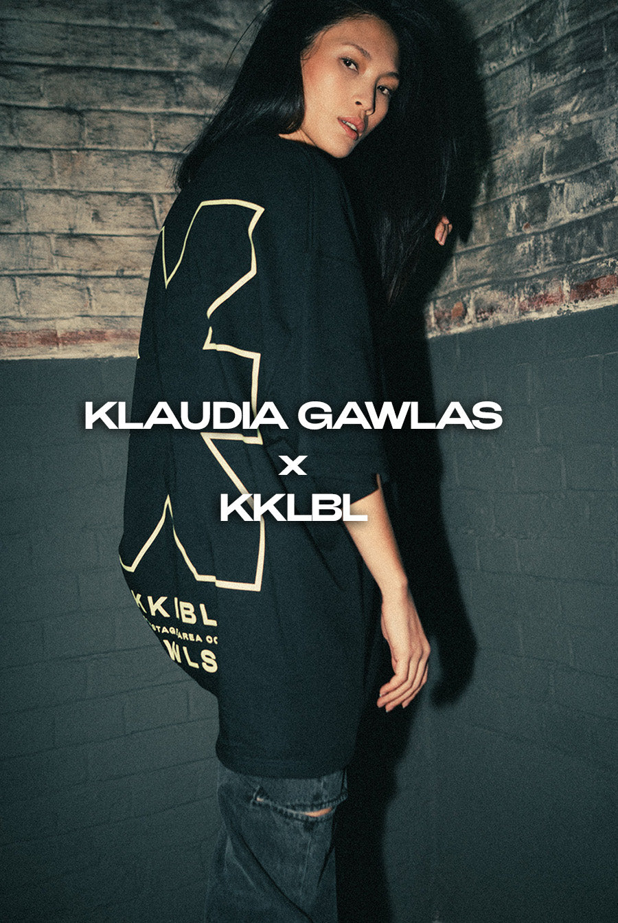 Ganzkörperaufnahme: Seitliche Rückenansicht einer Frau im schwarzen T-Shirt mit Neon-Logo aus GWLS x KKLBL Collection 