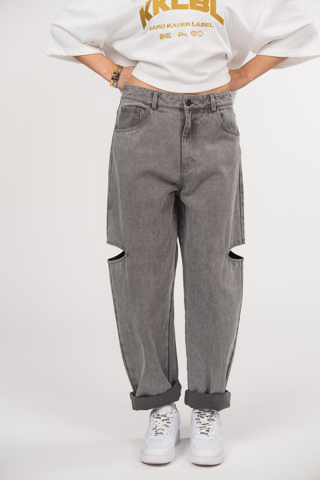 Ein Model trägt eine graue Cut-out-Jeans aus der No Hustle Culture Kollektion mit umgeschlagenem Saum, kombiniert mit weißen Sneakern