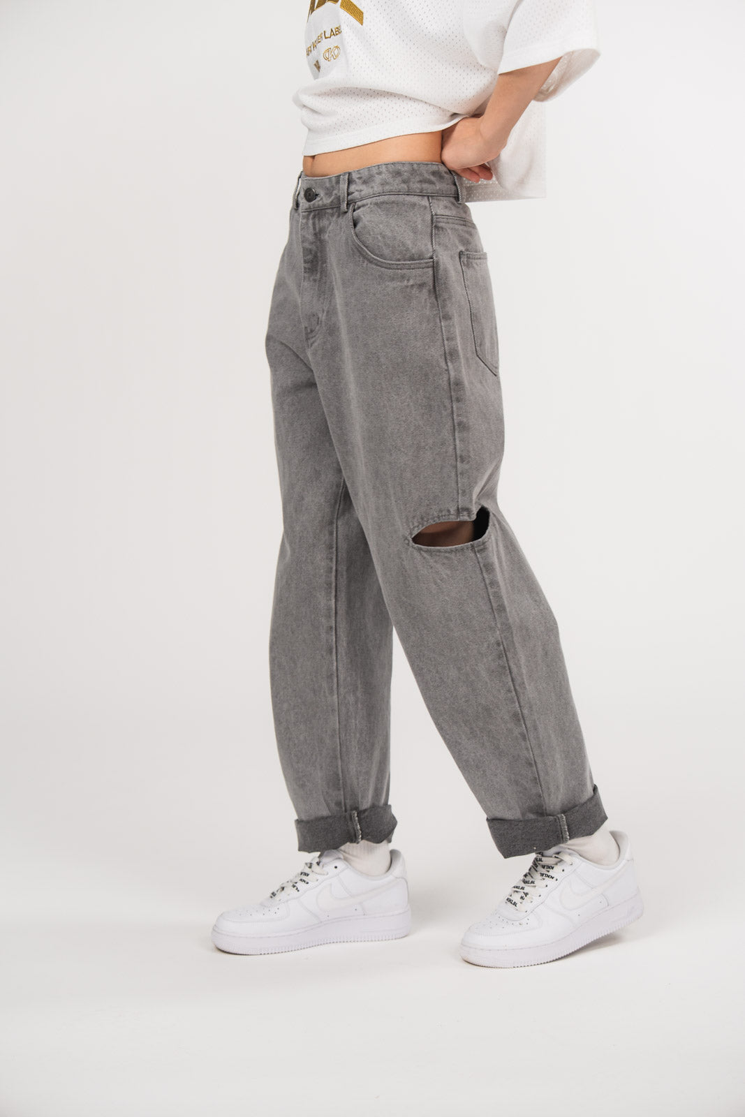 Ein Model trägt eine graue Cut-out-Jeans aus der No Hustle Culture Kollektion mit umgeschlagenem Saum, kombiniert mit weißen Sneakern