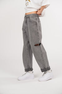 Ein Model trägt eine graue Cut-out-Jeans aus der No Hustle Culture Kollektion mit umgeschlagenem Saum, kombiniert mit weißen Sneakern