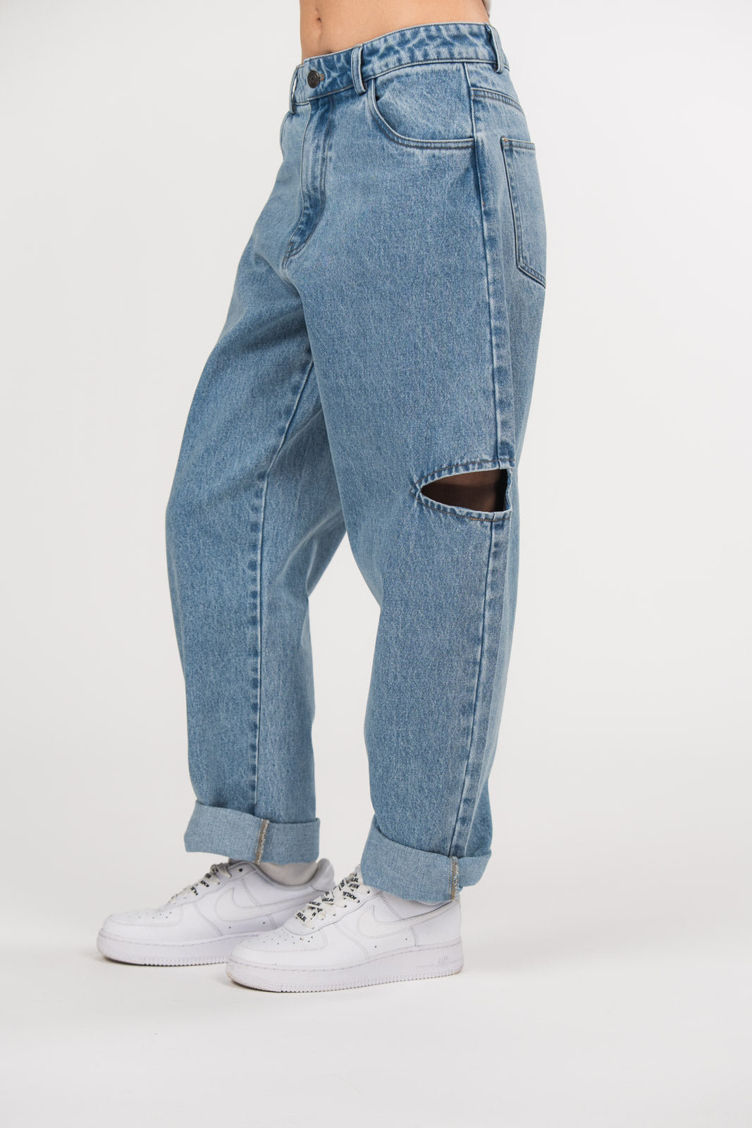 Ein Model trägt eine hellblaue Cut-out-Jeans aus der No Hustle Culture Kollektion mit umgeschlagenem Saum, kombiniert mit weißen Sneakern