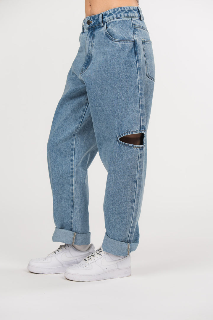 Ein Model trägt eine hellblaue Cut-out-Jeans aus der No Hustle Culture Kollektion mit umgeschlagenem Saum, kombiniert mit weißen Sneakern