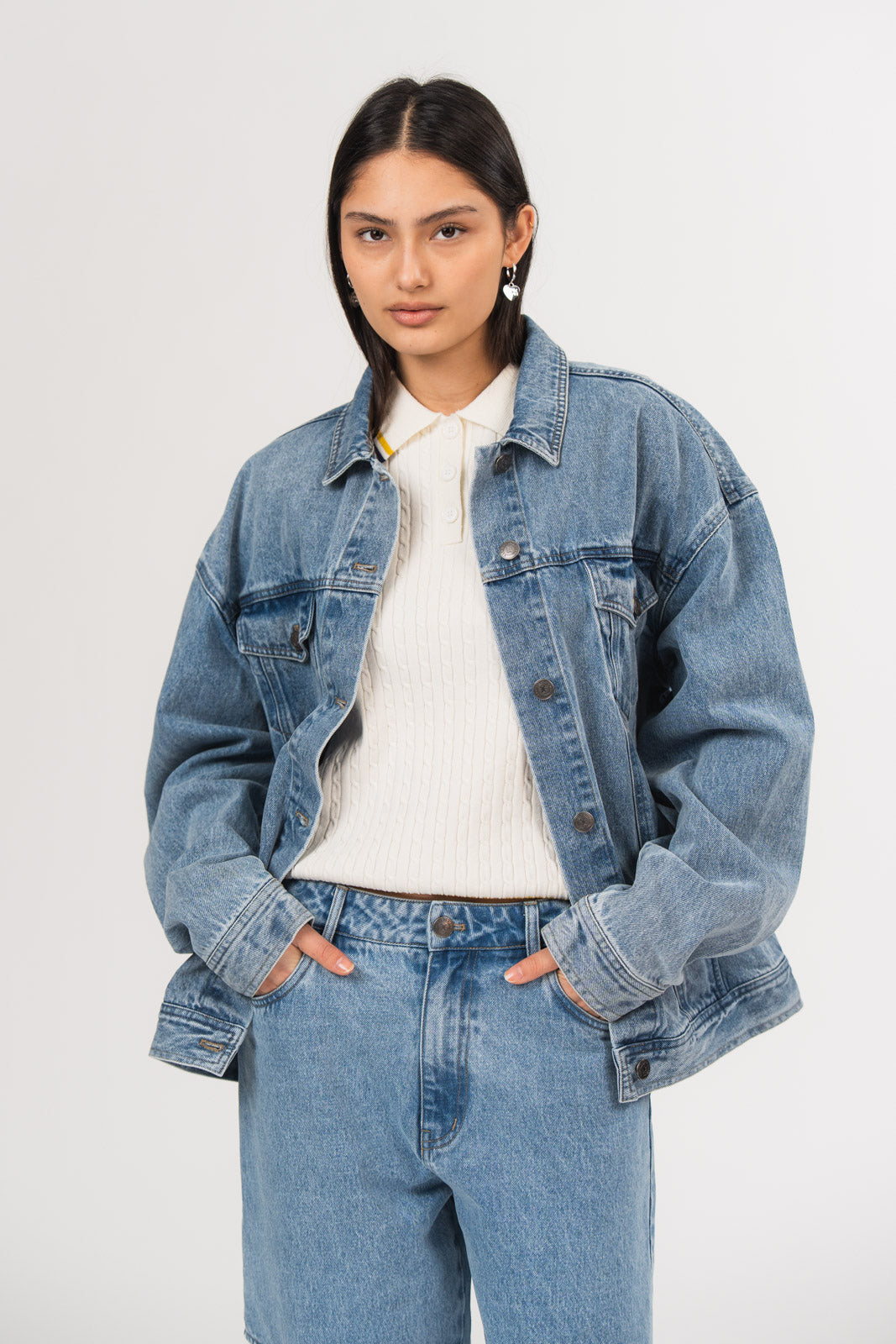 Ein Model trägt eine blaue Denimjacke und eine blaue Jeans aus der No Hustle Culture Kollektion, kombiniert mit einem Strick-Poloshirt mit Kragen