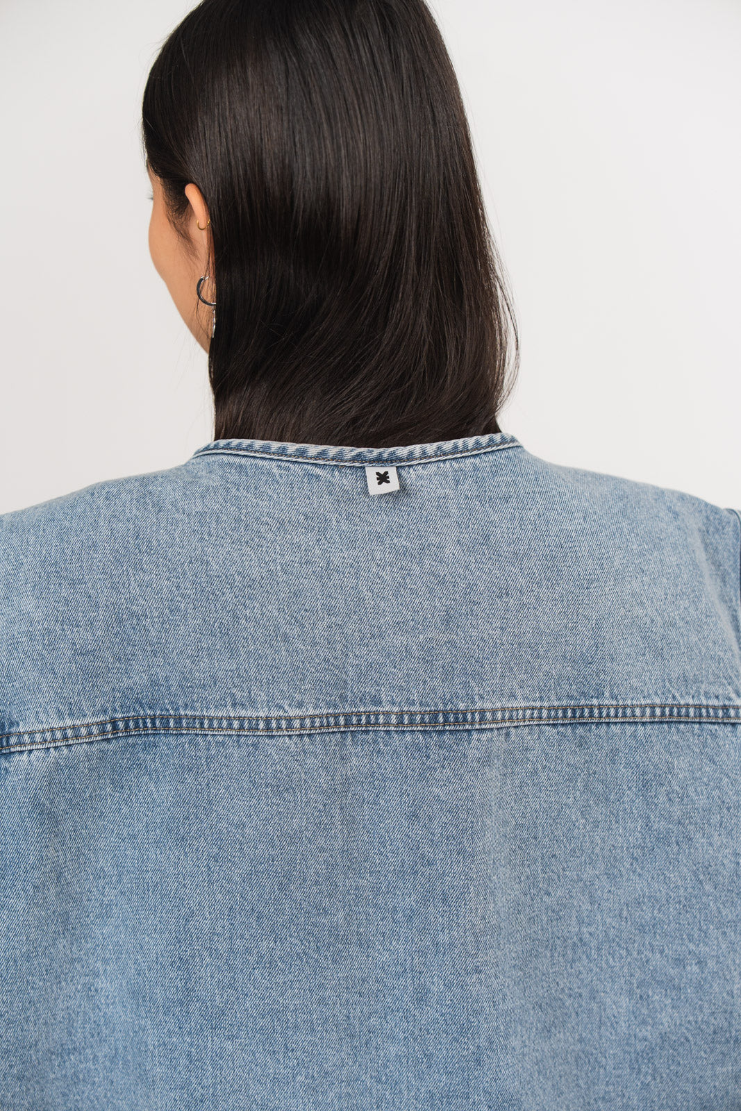 Detailansicht der Rückseite einer blauen Denimweste aus der No Hustle Culture Kollektion mit kleinem Logoflag hinten