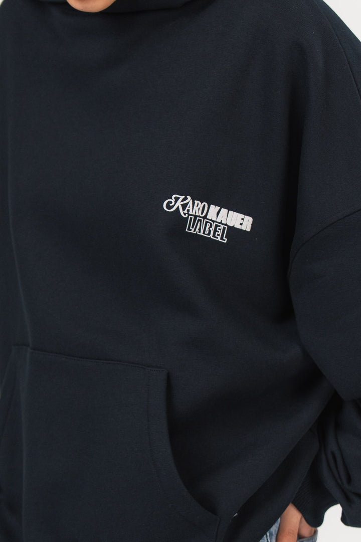 Detailansicht eines dunkelblauen Oversize-Hoodies aus der No Hustle Culture Kollektion mit kleinem weißen „KARO KAUER LABEL“-Print auf der Brust