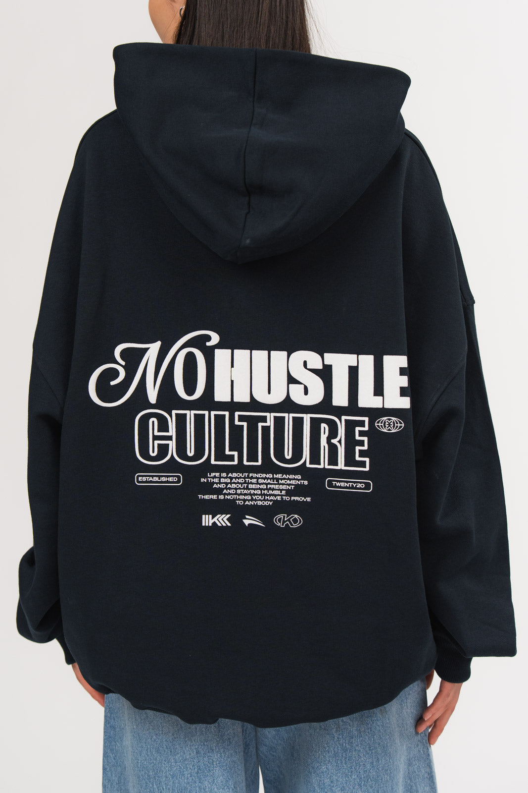 Ein Model, von hinten gezeigt, trägt einen dunkelblauen Oversize-Hoodie aus der No Hustle Culture Kollektion mit Kapuze und großem weißen Rückenprint aus dem Schriftzug „No Hustle Culture“, kleinem Textblock und Logo-Elementen