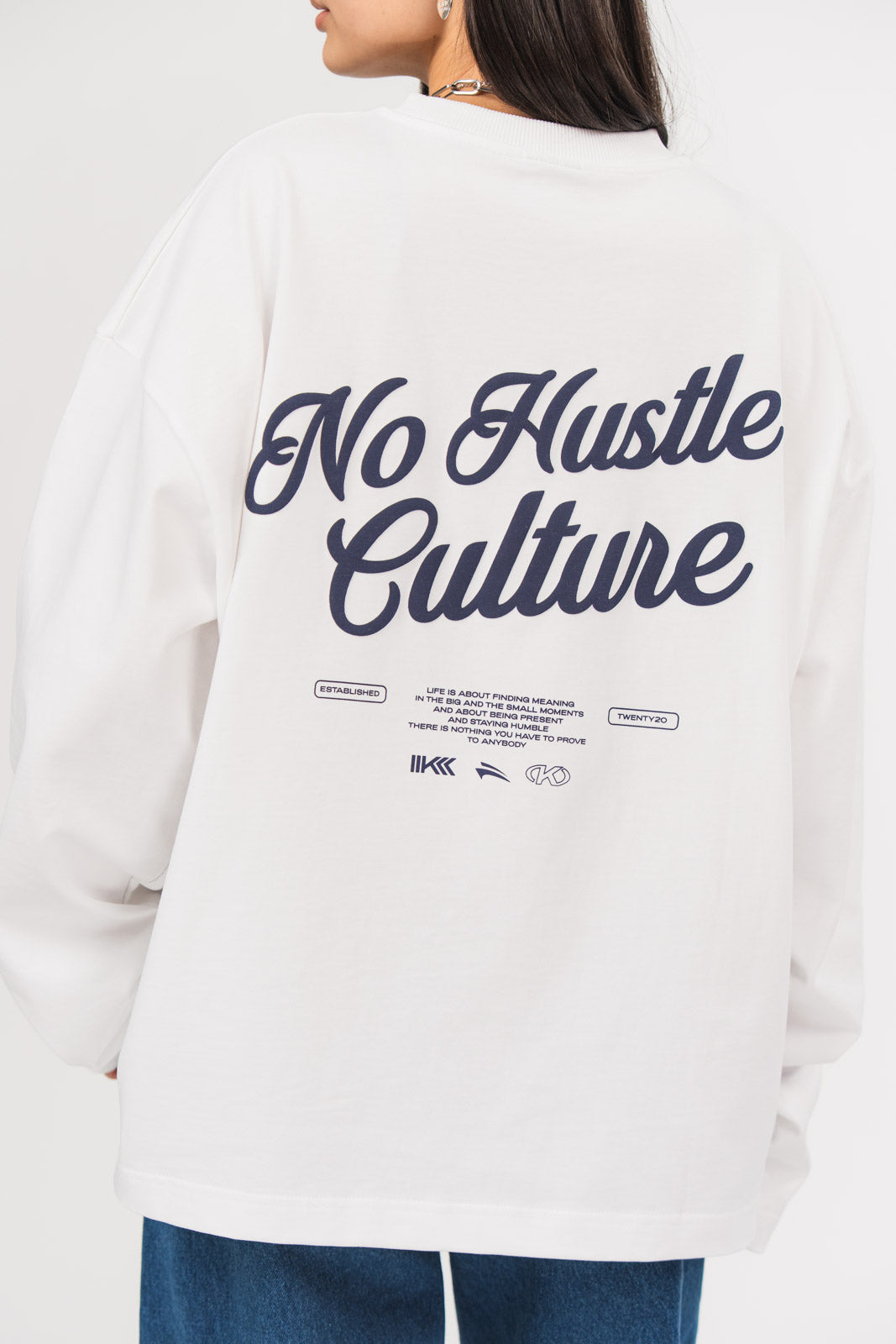 Rückansicht eines weißen Longsleeves aus der No Hustle Culture Kollektion mit großem dunkelblauen Rückenprint aus dem Schriftzug „No Hustle Culture“, kleinem Textblock und Logo-Elementen
