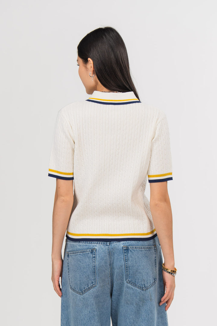 Ein Model, von hinten gezeigt, trägt ein offwhite Strick-Poloshirt mit weißem Kragen, gelben und dunkelblauen Kontraststreifen an Kragen, Ärmeln und Saum aus der No Hustle Culture Kollektion, kombiniert mit einer blauen Jeans 