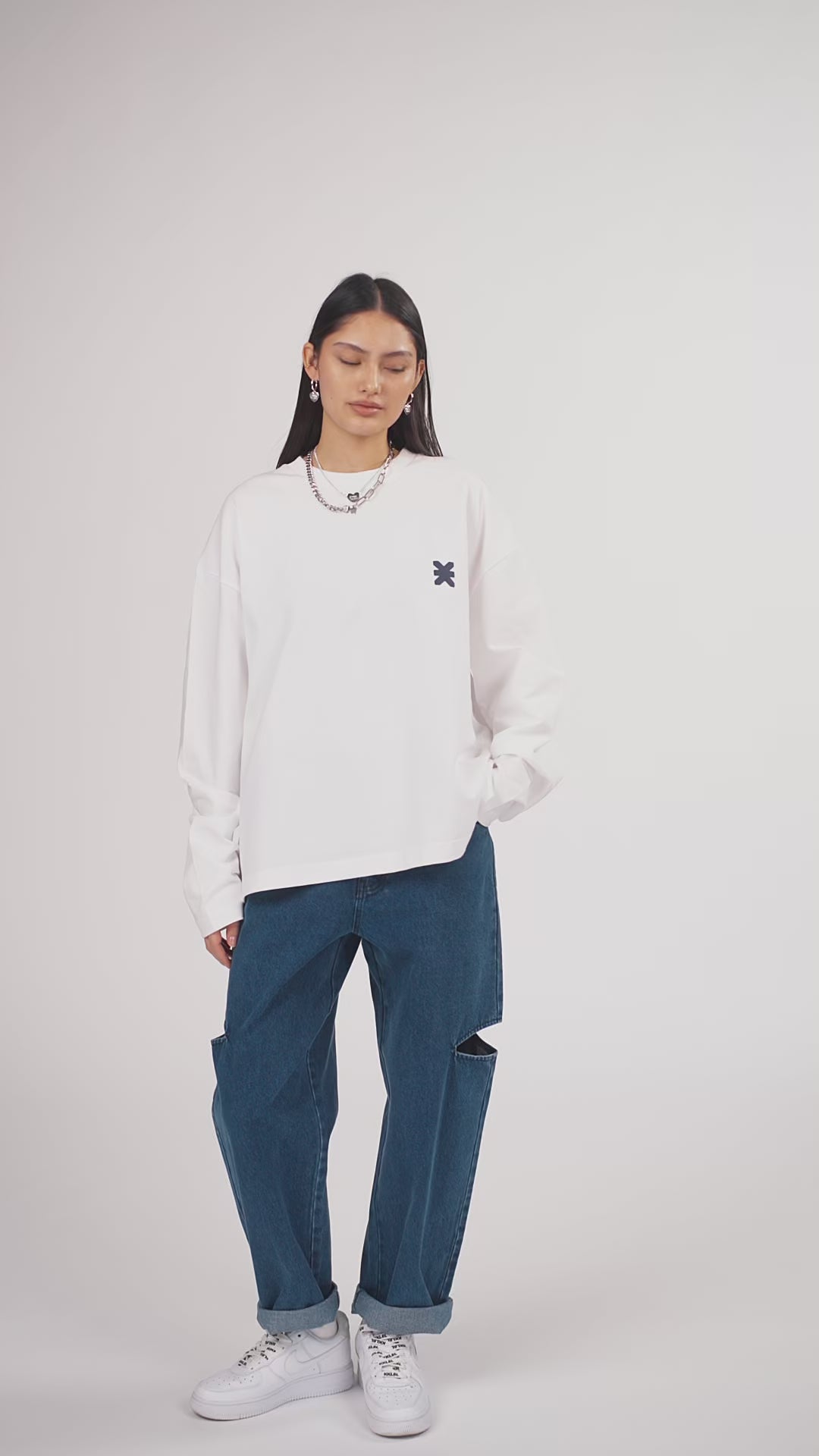 Ein Model in Ganzkörperansicht, das den Look in Bewegung aus verschiedenen Perspektiven zeigt, trägt ein hellgraues Oversize-Sweatshirt mit verschiedenen Prints, kombiniert mit einer blauen Cut-out-Jeans aus der No Hustle Culture Kollektion, weißen Sneakern und silberfarbenem Schmuck