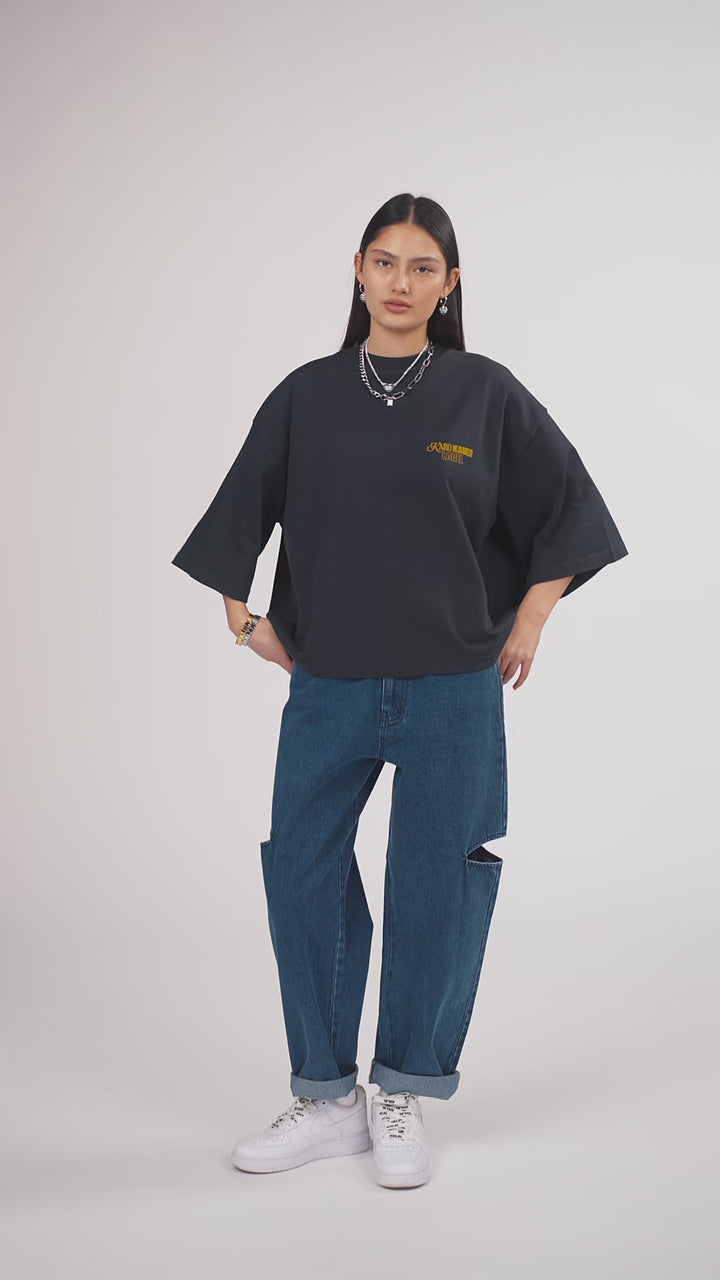Ein Model in Ganzkörperansicht, das den Look in Bewegung aus verschiedenen Perspektiven zeigt, trägt ein hellgraues Oversize-Sweatshirt mit verschiedenen gelbfarbigen Prints, kombiniert mit einer blauen Cut-out-Jeans aus der No Hustle Culture Kollektion, weißen Sneakern und silberfarbenem Schmuck