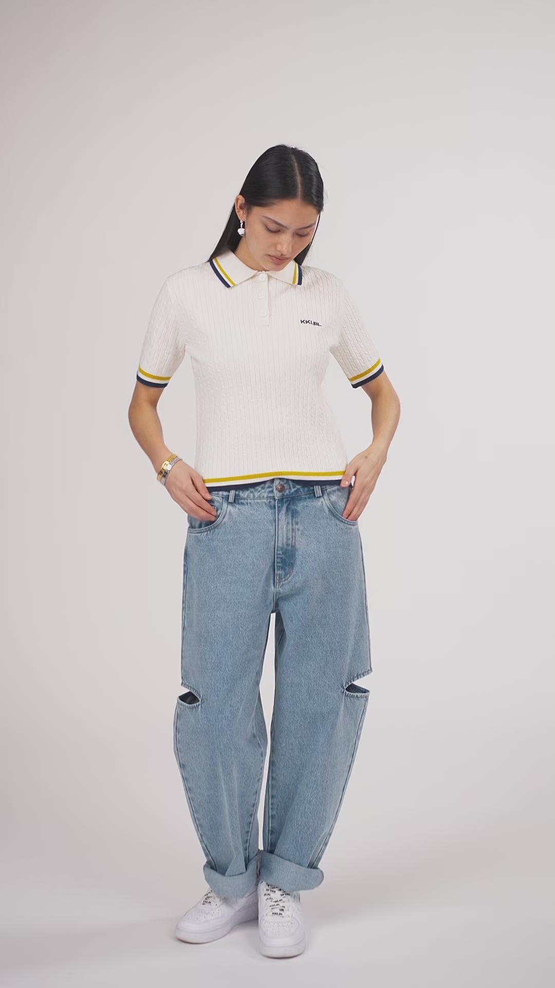 Ein Model in Ganzkörperansicht, das den Look in Bewegung aus verschiedenen Perspektiven zeigt, trägt ein offwhite Strick-Poloshirt und eine hellblaue Cut-out-Jeans aus der No Hustle Culture Kollektion, kombiniert mit weißen Sneakern und silberfarbenem Schmuck