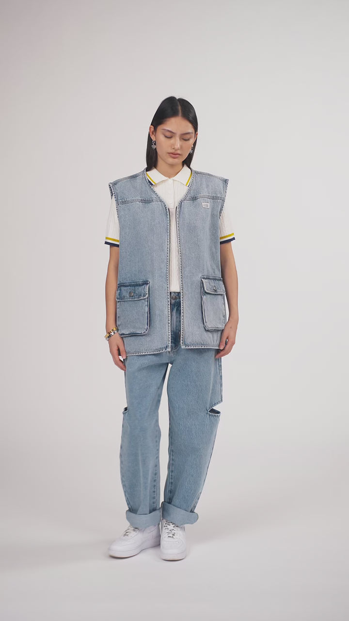 Ein Model in Ganzkörperansicht, das den Look in Bewegung aus verschiedenen Perspektiven zeigt, trägt eine blaue Denimweste und eine blaue Cut-out-Jeans aus der No Hustle Culture Kollektion, kombiniert mit einem offwhite Strick-Poloshirt, weißen Sneakern und silberfarbenem Schmuck